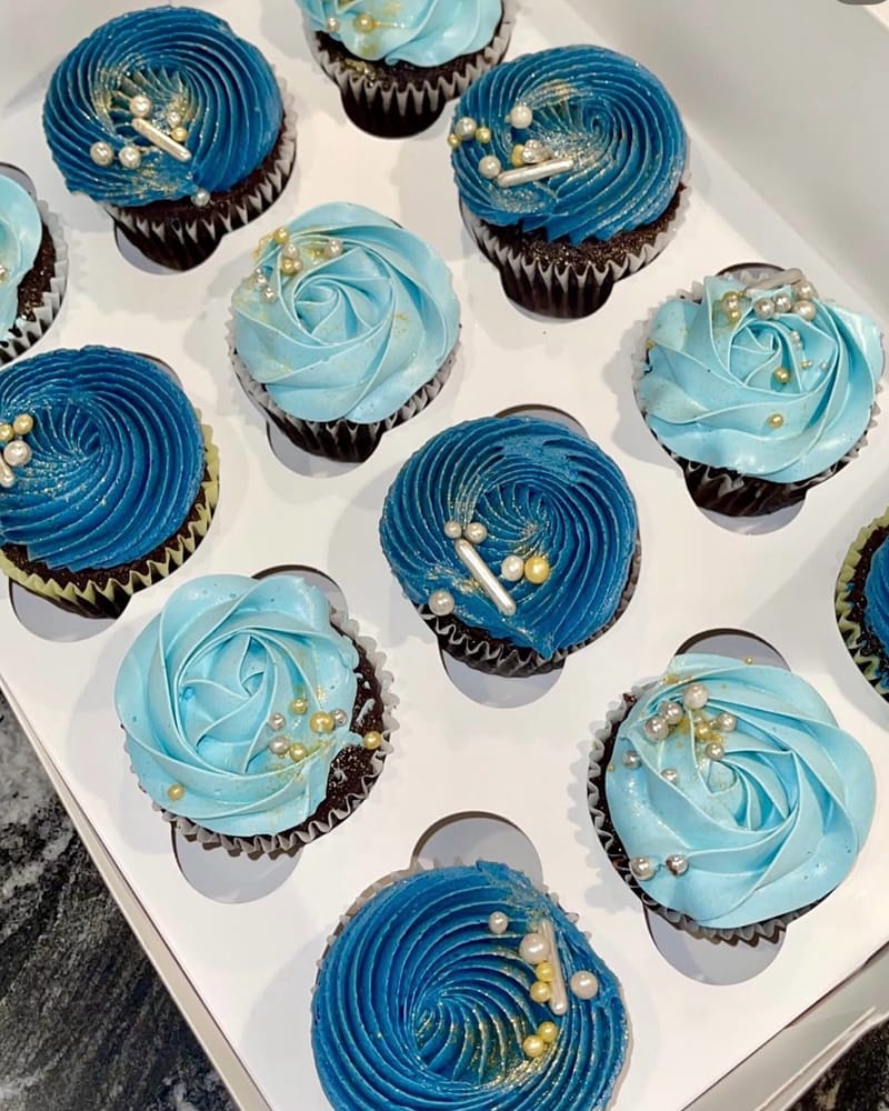Close-up of chocolate cupcakes piped with light and dark blue swirls and finished with silver and gold pearl sprinkles