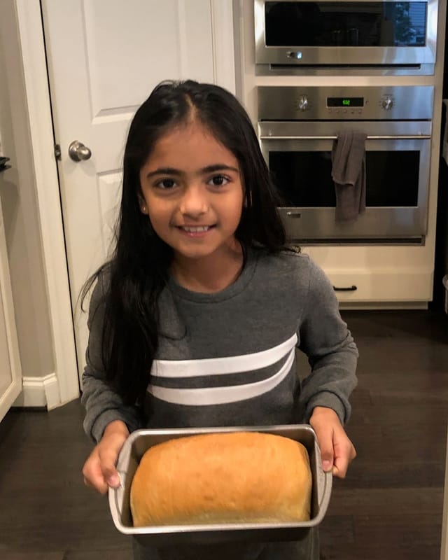 Elina as a young child, smiling and holding a freshly baked loaf of bread in its pan
