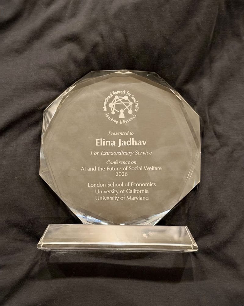 Crystal award engraved: Presented to Elina Jadhav, For Extraordinary Service, Conference on AI and the Future of Social Welfare 2026, London School of Economics, University of California, University of Maryland